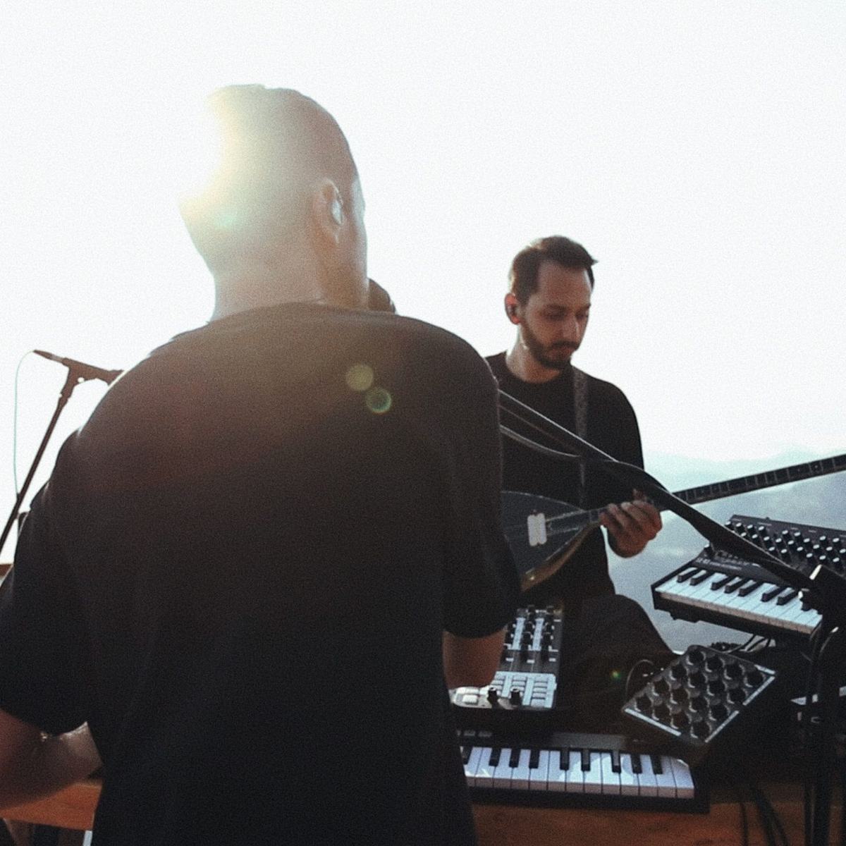 YėY performing outdoors in bright daylight, playing the saz